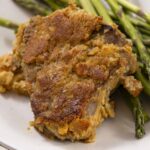 Succulent baked chicken thigh with crispy golden crust served with fresh roasted asparagus on a white plate. Perfect for delicious homemade comfort food and healthy side dish options.