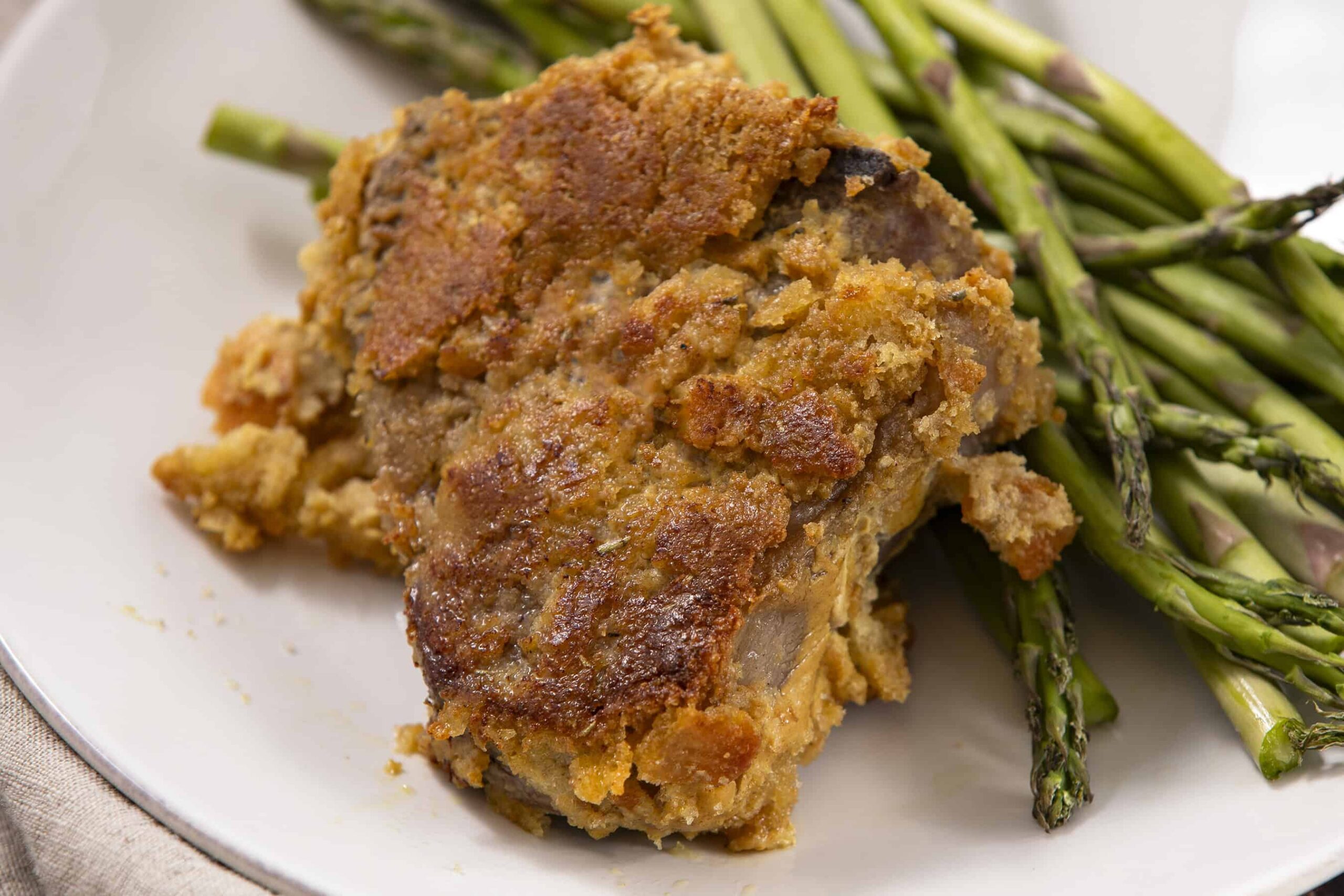 Succulent baked chicken thigh with crispy golden crust served with fresh roasted asparagus on a white plate. Perfect for delicious homemade comfort food and healthy side dish options.