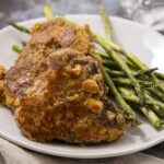 Juicy baked chicken thigh with a golden crispy coating served with fresh grilled asparagus on a white plate. Perfect for a healthy and flavorful meal.