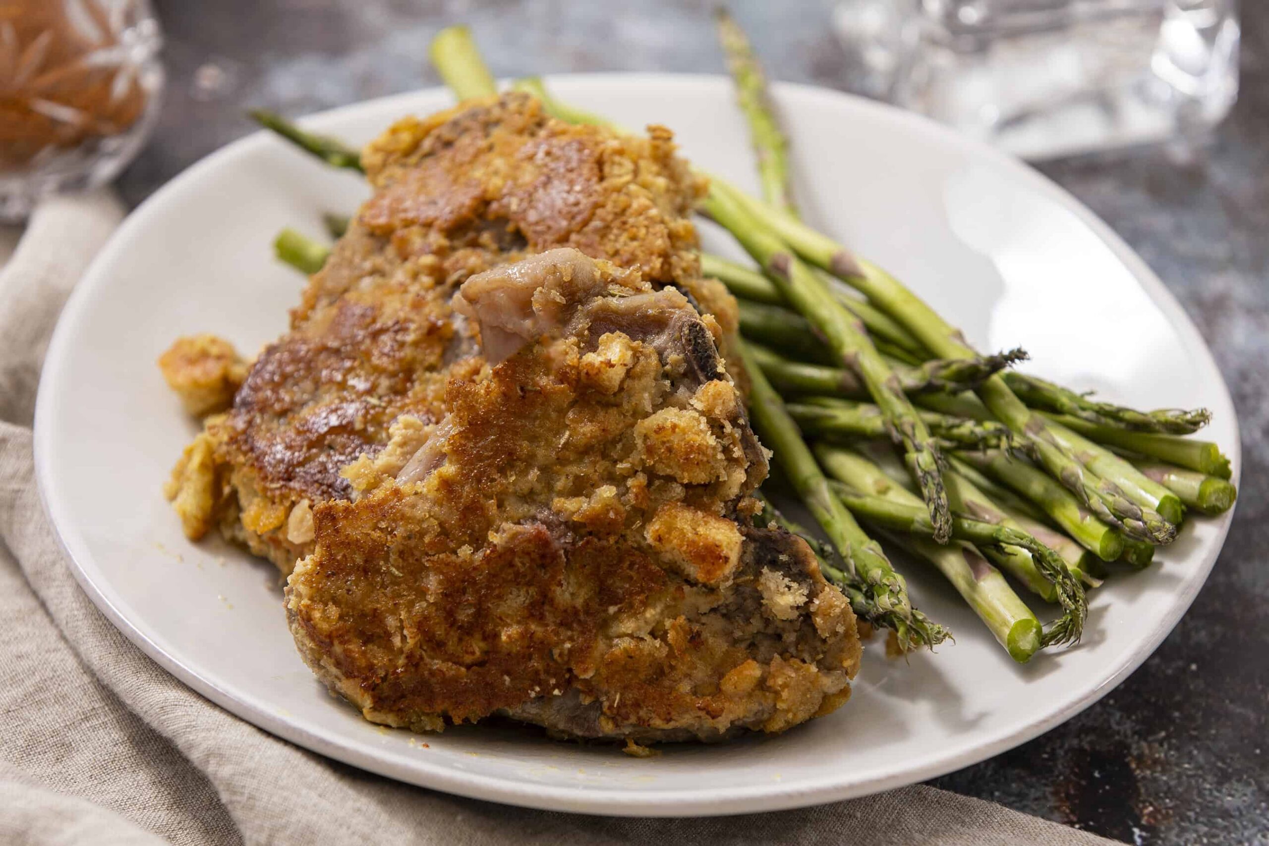 Juicy baked chicken thigh with a golden crispy coating served with fresh grilled asparagus on a white plate. Perfect for a healthy and flavorful meal.