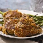 Baked chicken thigh with crispy breading served with fresh green asparagus on a white plate. Perfect for a healthy dinner or springtime meal.