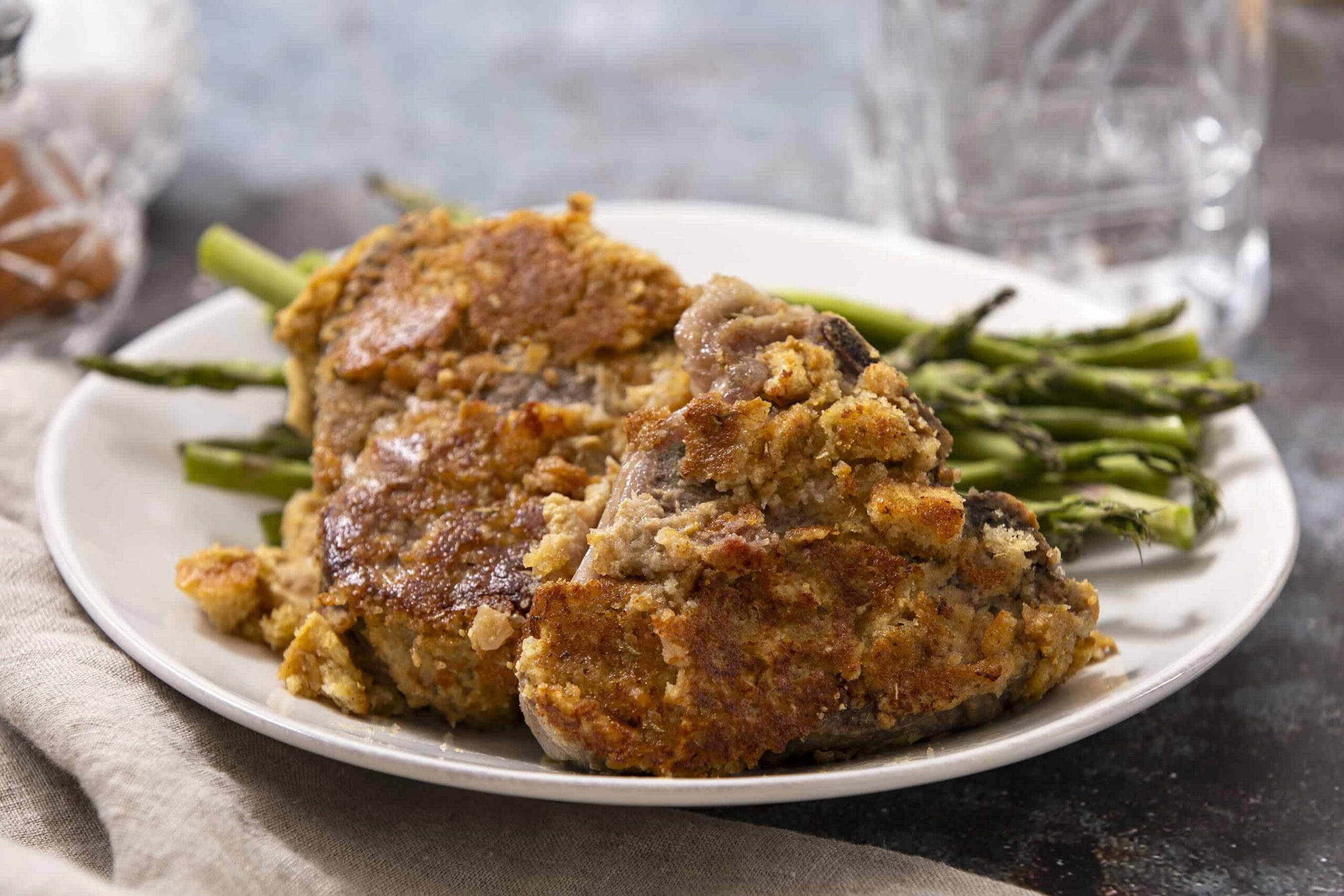 Baked chicken thigh with crispy breading served with fresh green asparagus on a white plate. Perfect for a healthy dinner or springtime meal.