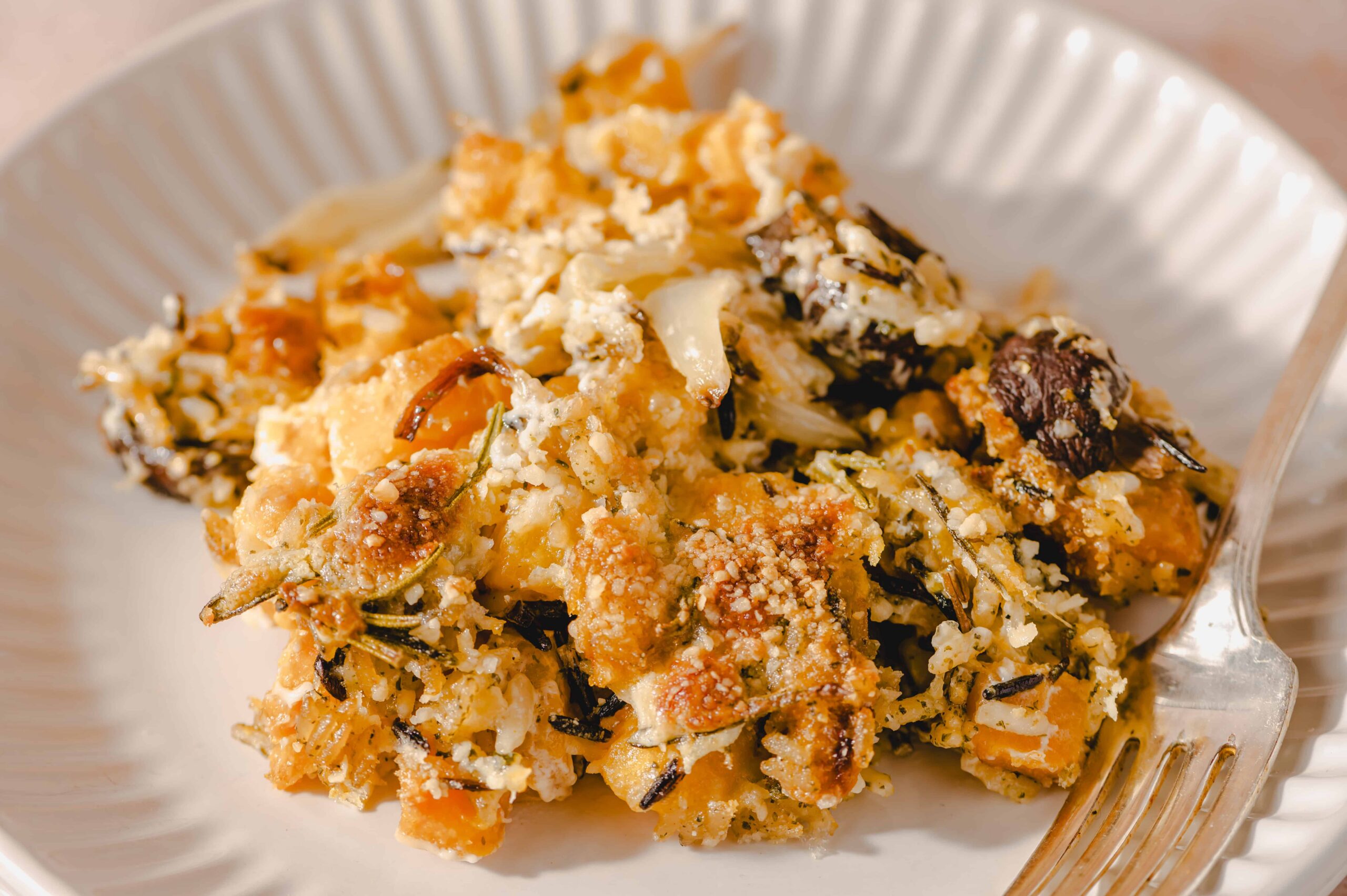 Creamy roasted vegetable casserole with cheese, herbs, and breadcrumbs on a white plate, served with a fork, perfect for vegetarian meal ideas.