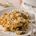 Creamy wild mushroom risotto with grated cheese and fresh herbs on a white plate. Perfect comfort food recipe, served with a silver fork on a textured napkin.