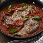 Succulent sliced beef in a rich tomato sauce garnished with fresh basil, served in a black skillet for an authentic Italian-style meat dish. Perfect for pasta or rice accompaniments.