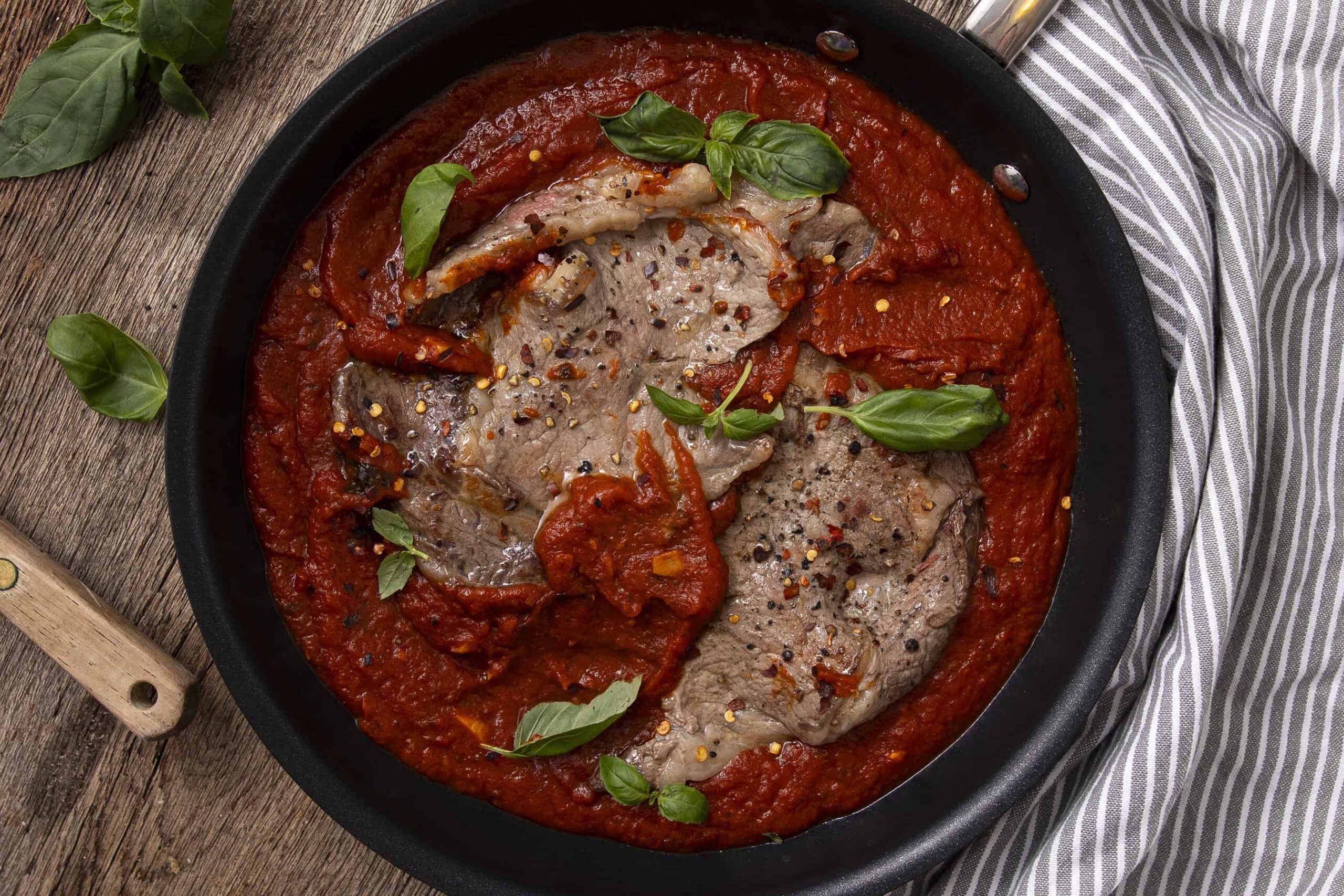 Juicy pork chops cooked in rich tomato sauce garnished with fresh basil and red pepper flakes, served in a black skillet for a flavorful and hearty meal.