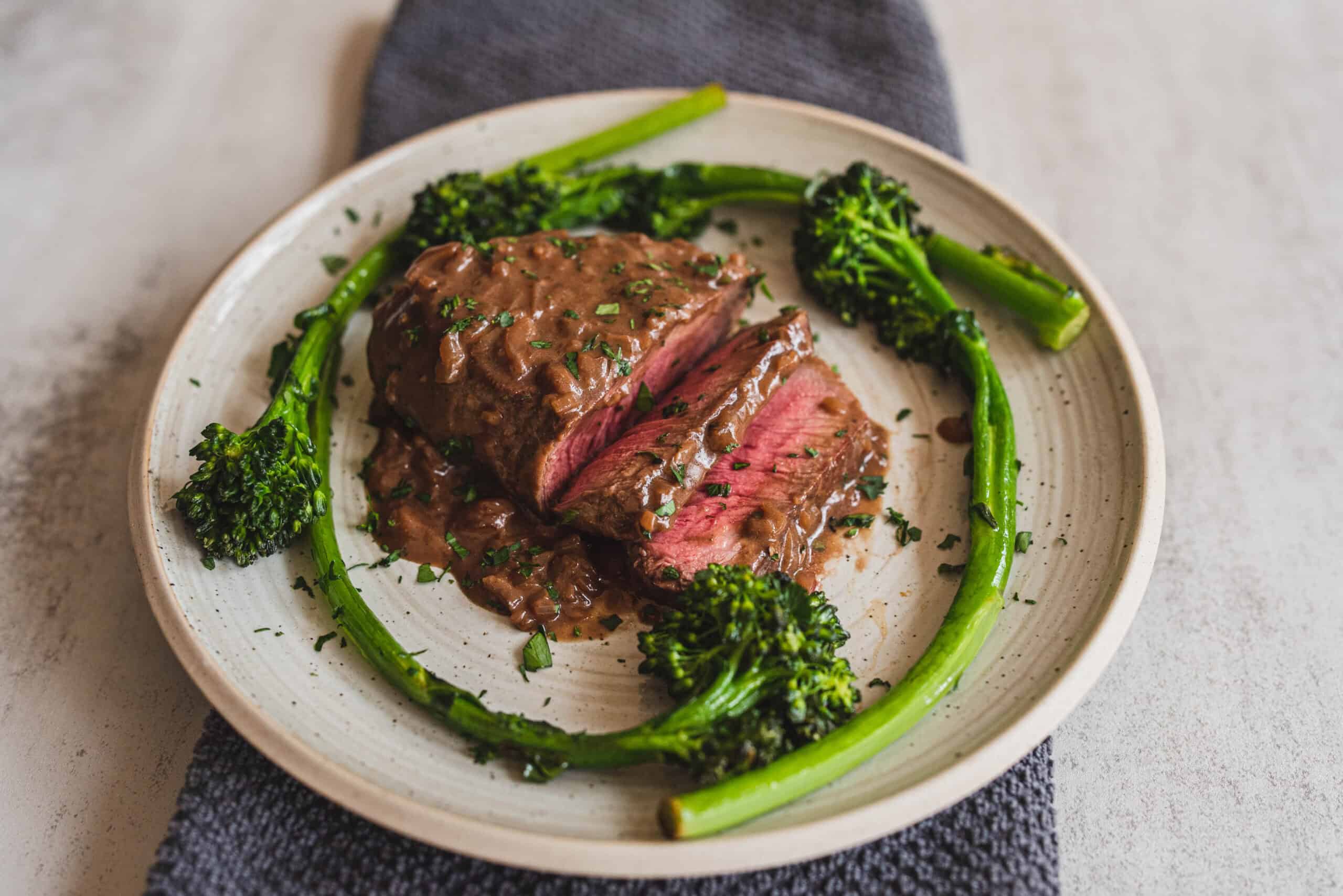 Juicy beef steak with mushroom gravy served with fresh steamed broccoli on a ceramic plate. Perfect for a delicious, hearty, and healthy dinner.