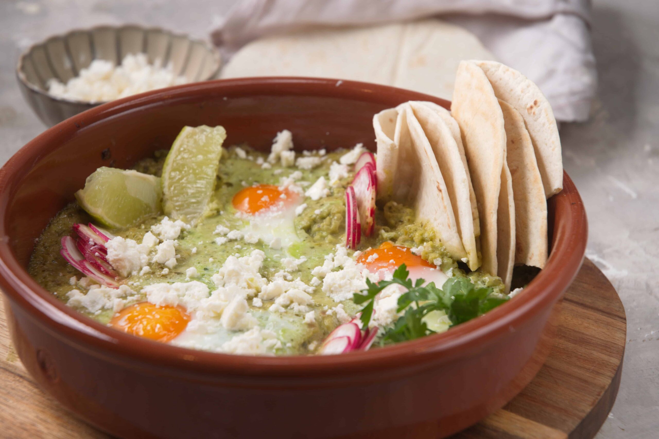 Fresh huevos divorciados served with avocado, radish, shredded cheese, and tortillas in a traditional Mexican clay bowl. Perfect for breakfast or brunch, offering authentic flavors and colors.