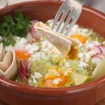 Fried eggs in a traditional Mexican dish served in a terracotta bowl with radishes, lemon, fresh herbs, and crispy tortillas, showcasing authentic Mexican breakfast comfort food.