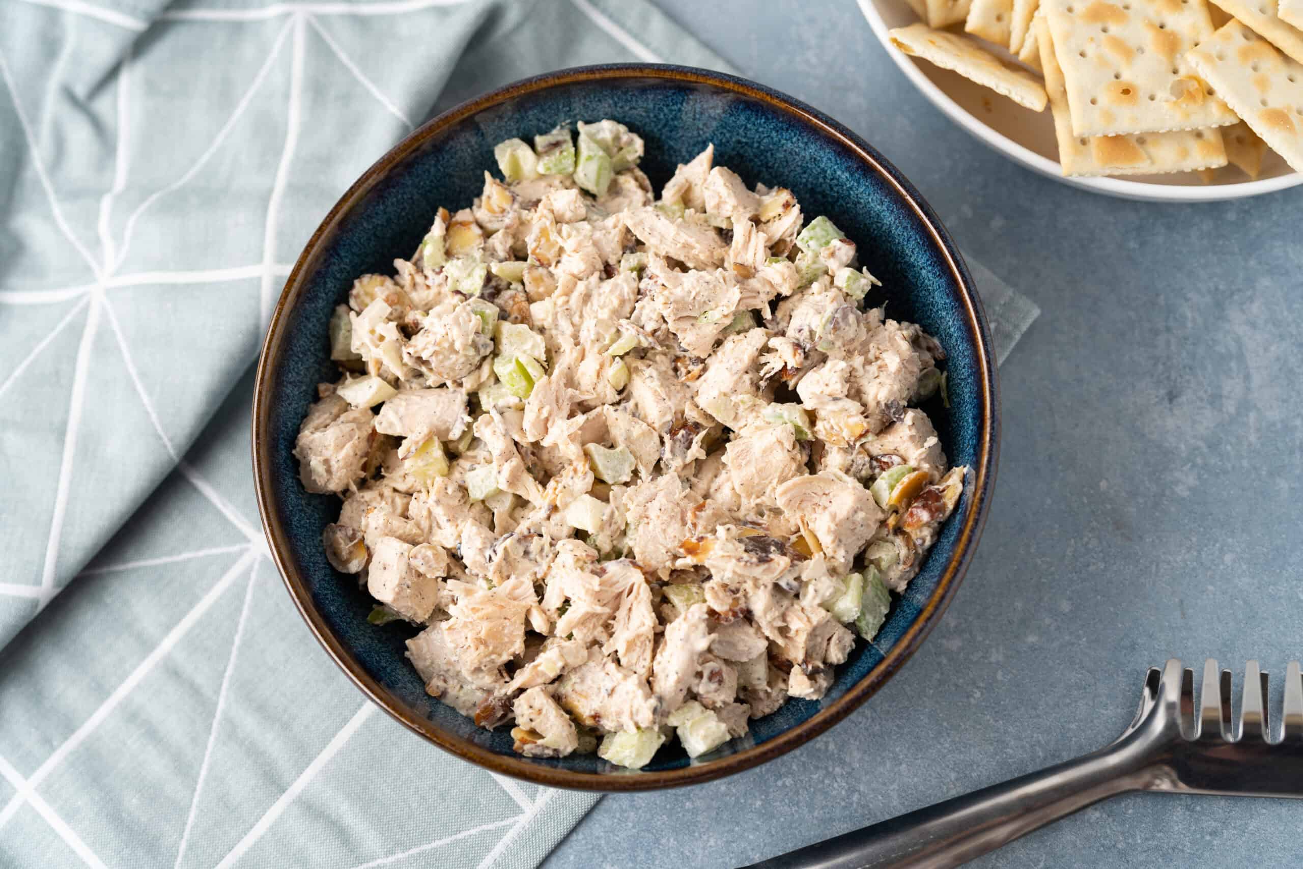 Creamy chicken salad with chopped celery and herbs in a blue ceramic bowl, served as a delicious lunch or appetizer. Perfect for picnics, sandwiches, or light meals. Made with tender cooked chicken and mayonnaise.
