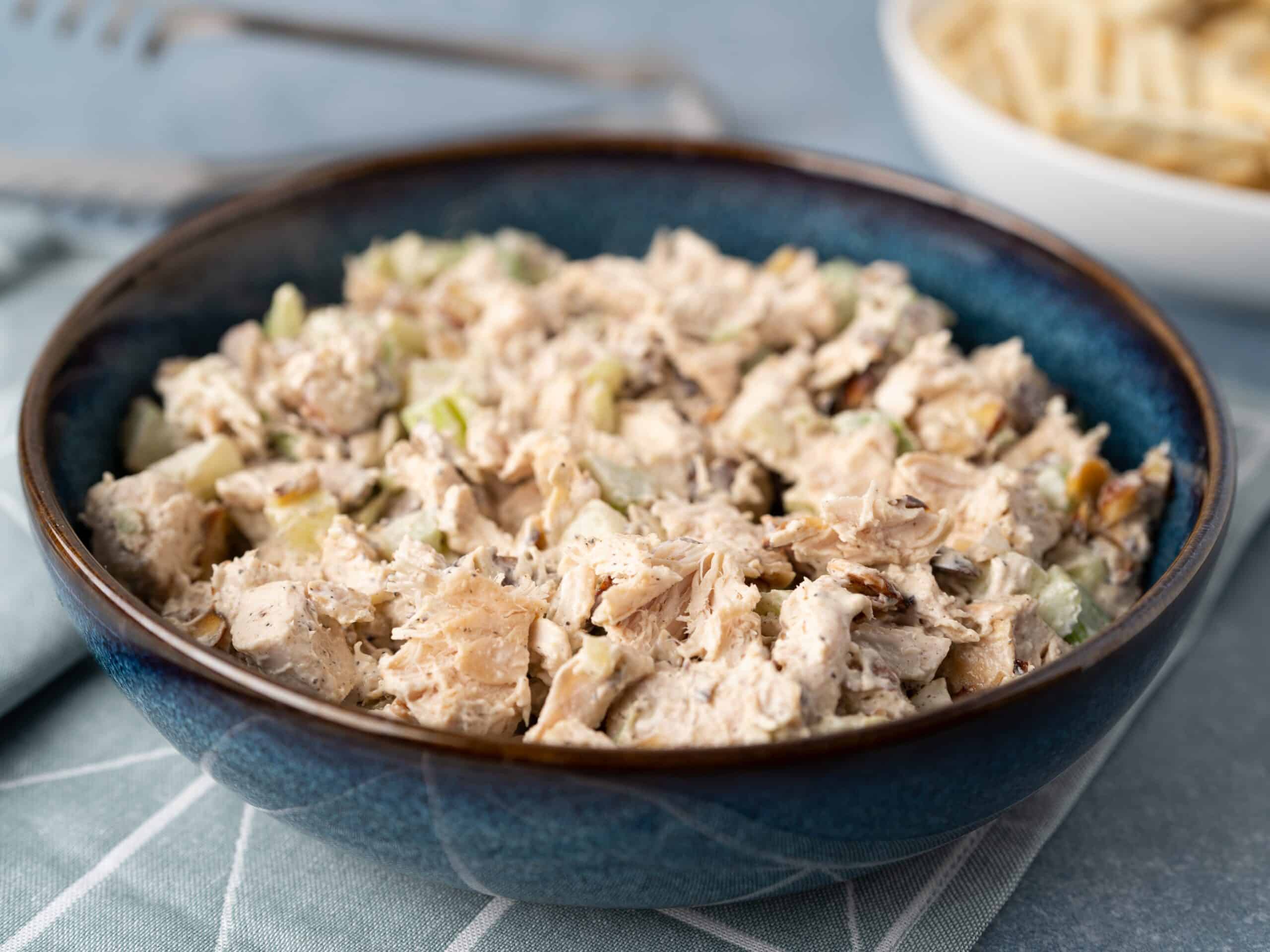 Creamy chicken salad with chopped celery and herbs in a blue ceramic bowl, served as a savory appetizer or lunch option. Perfect for sandwiches or on its own, easy to make and full of flavor.