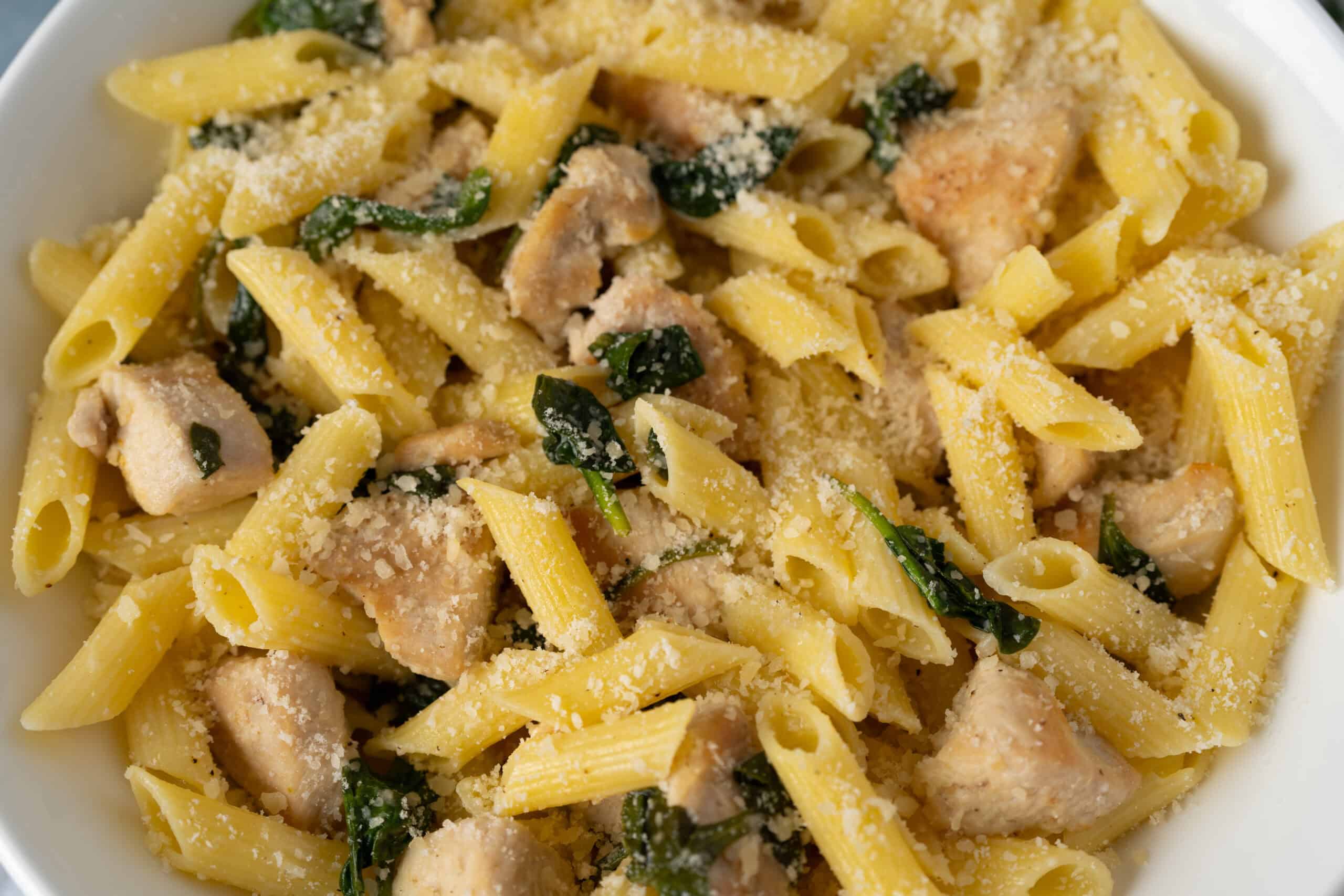Creamy chicken pasta with spinach, Parmesan cheese, and garlic, served in a white bowl, highlighting a delicious and hearty Italian-inspired meal perfect for weeknight dinners.