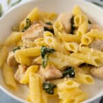 Creamy chicken pasta with spinach and grated Parmesan cheese on a white plate, served with a fork, fresh ingredients, and a colorful tablecloth. Perfect for quick weeknight dinners.