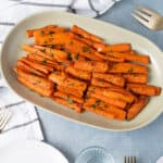 Roasted sweet potato fries garnished with chopped parsley on an elegant cream-colored platter. Perfect side dish for lunch or dinner, served with a simple and flavorful seasoning.