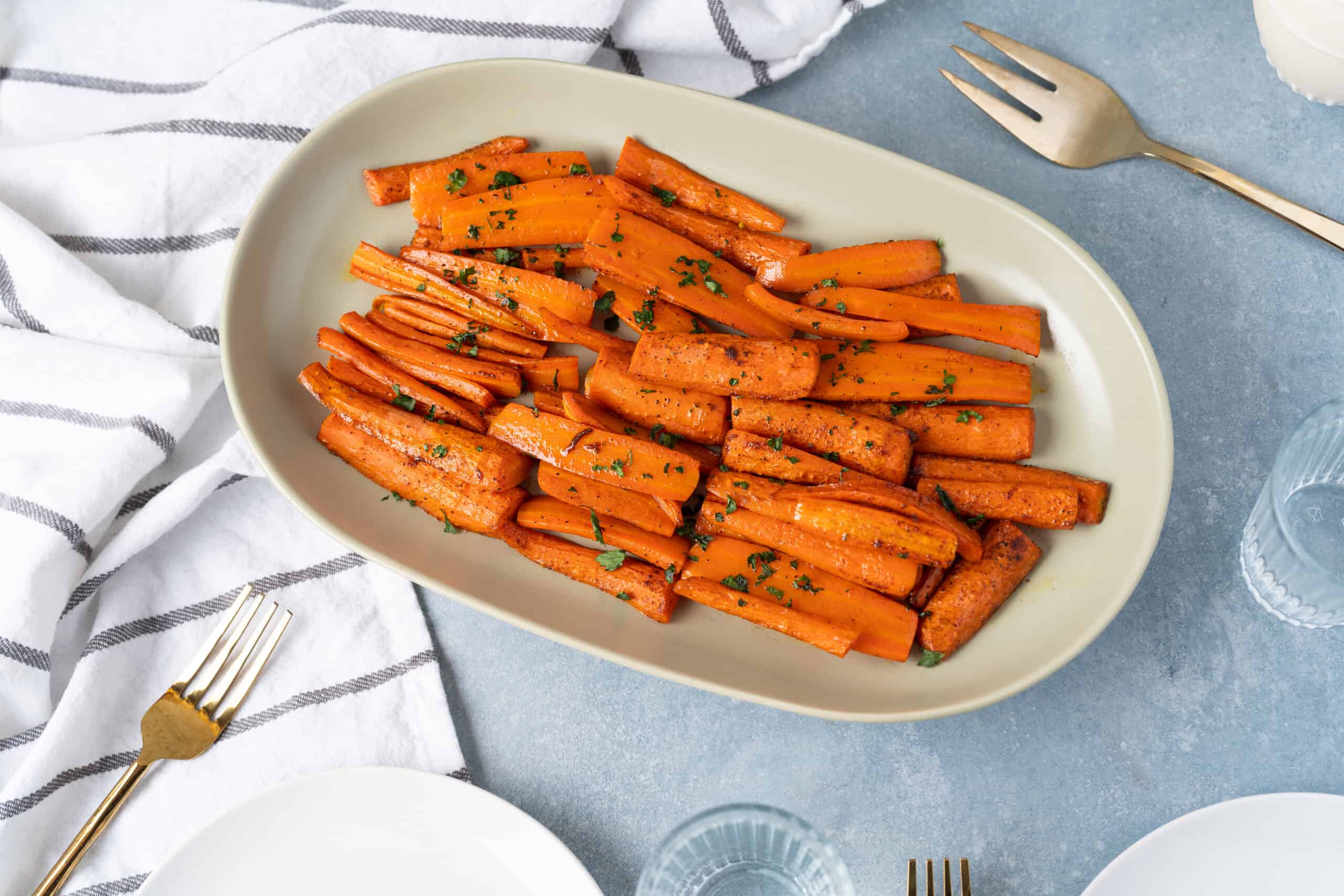 Roasted sweet potato fries garnished with chopped parsley on an elegant cream-colored platter. Perfect side dish for lunch or dinner, served with a simple and flavorful seasoning.
