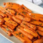 Roasted sweet potato fries garnished with chopped parsley served on a white oval platter.