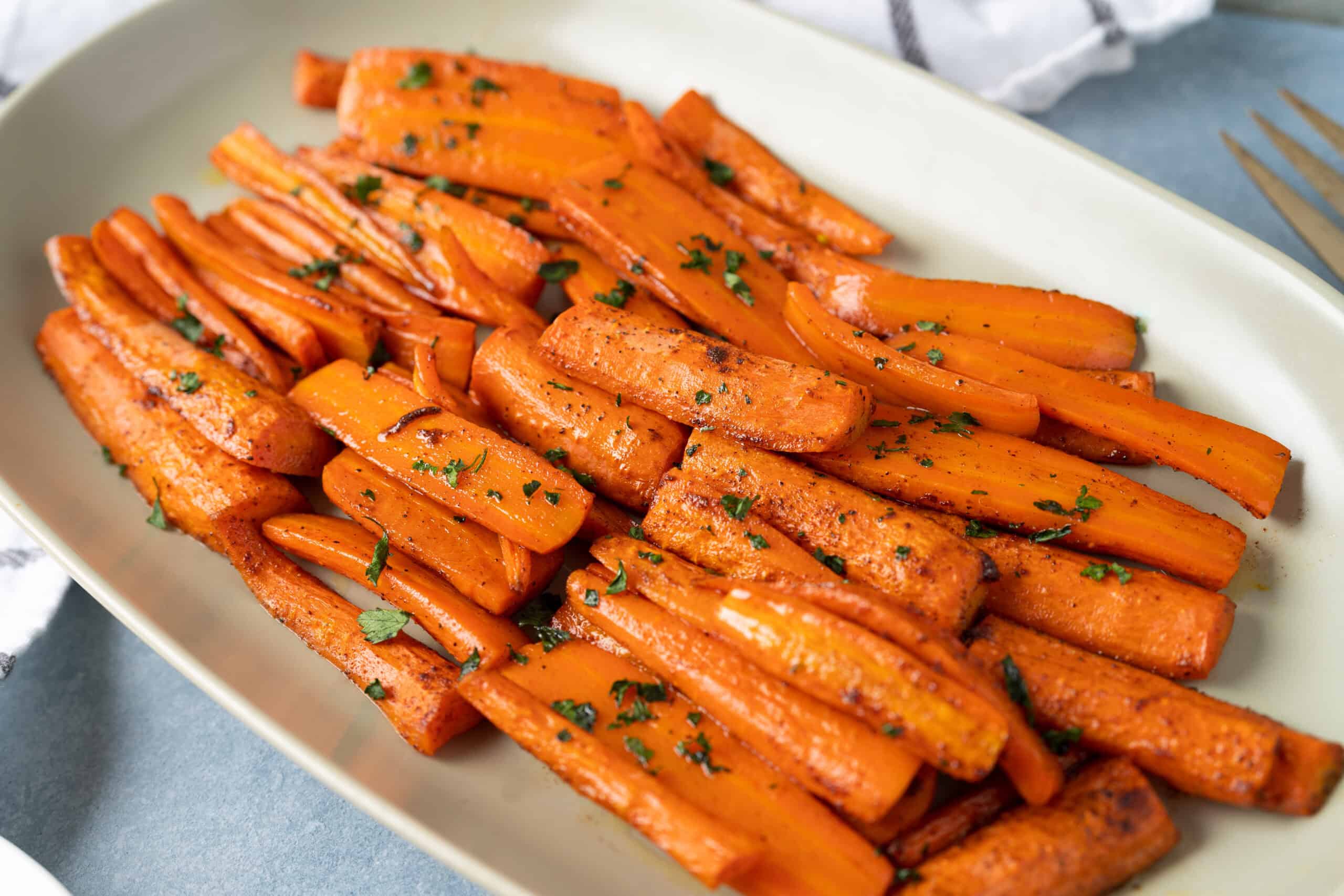 Roasted sweet potato fries garnished with chopped parsley served on a white oval platter.