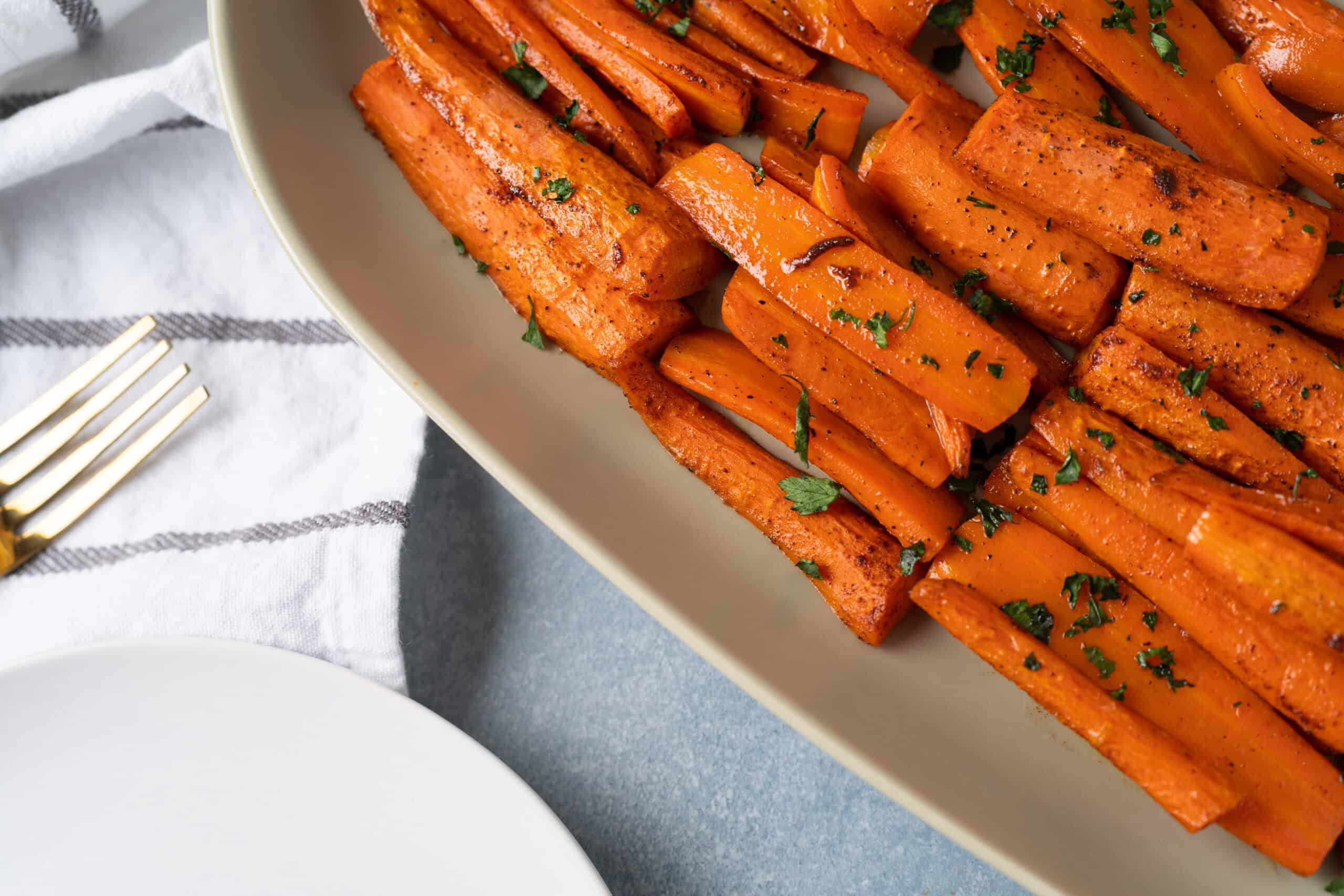 Roasted sweet potatoes seasoned with spices and garnished with herbs, served on a white dish for a healthy, flavorful side dish.