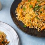 Stir-fried vegetable noodle dish with carrots, green onions, and bean sprouts on black and white plates, showcasing healthy vegetarian Asian cuisine.