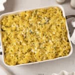 Creamy macaroni and cheese baked casserole dish topped with chopped herbs, served in a white baking dish for comfort food.