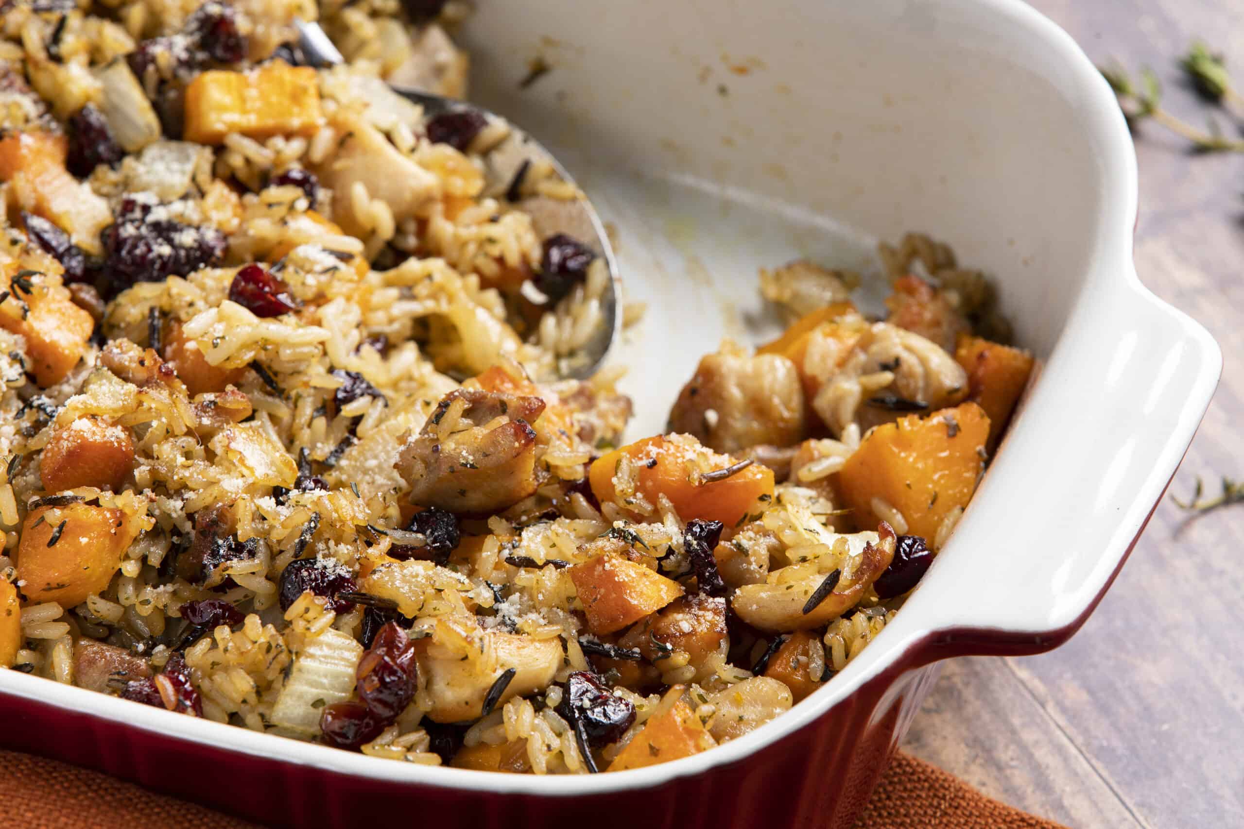 Creamy chicken and rice casserole with sweet potatoes, cranberries, and herbs in a white baking dish, ready for oven baking.