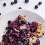 Fresh blueberry cobbler dessert with baked berries and crispy crust on a white plate.