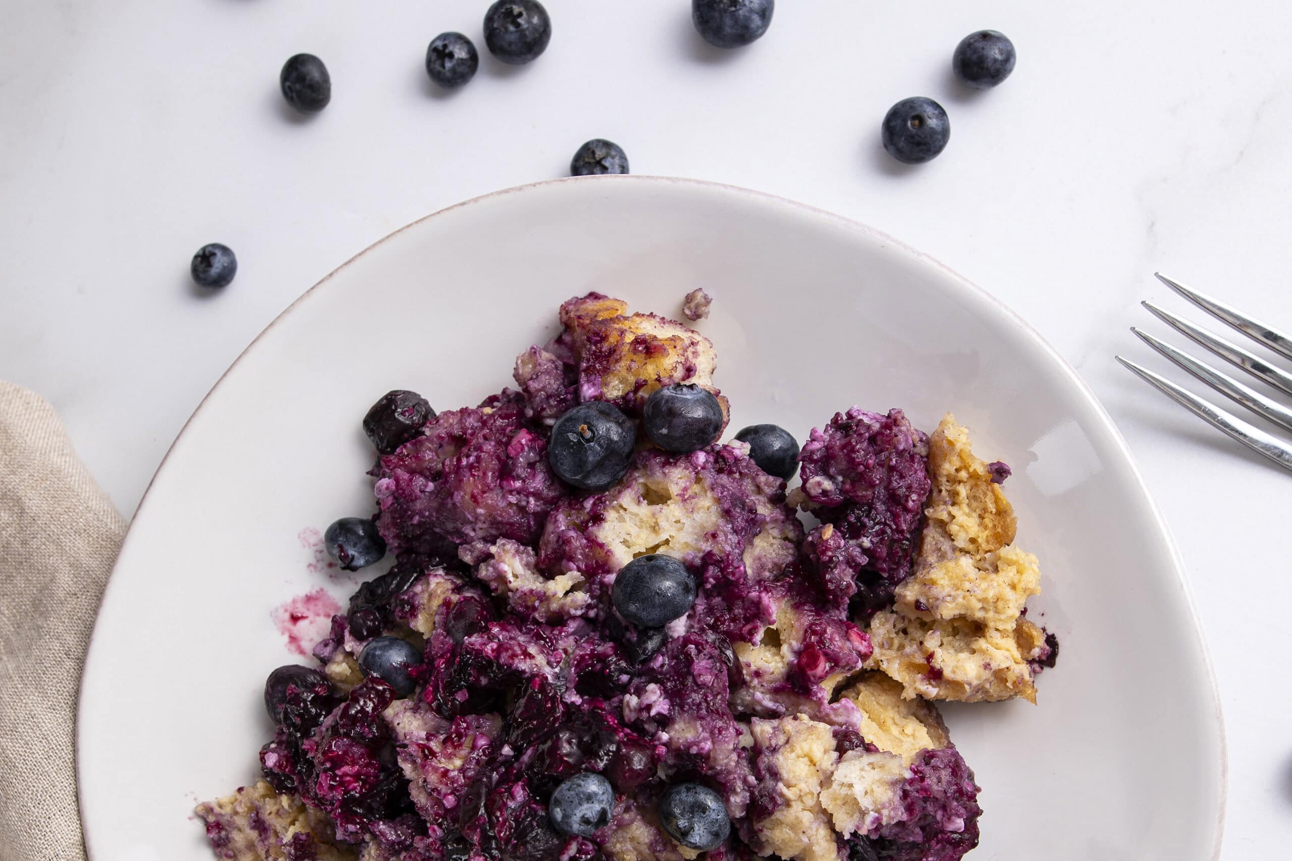Fresh blueberry cobbler dessert with baked berries and crispy crust on a white plate.