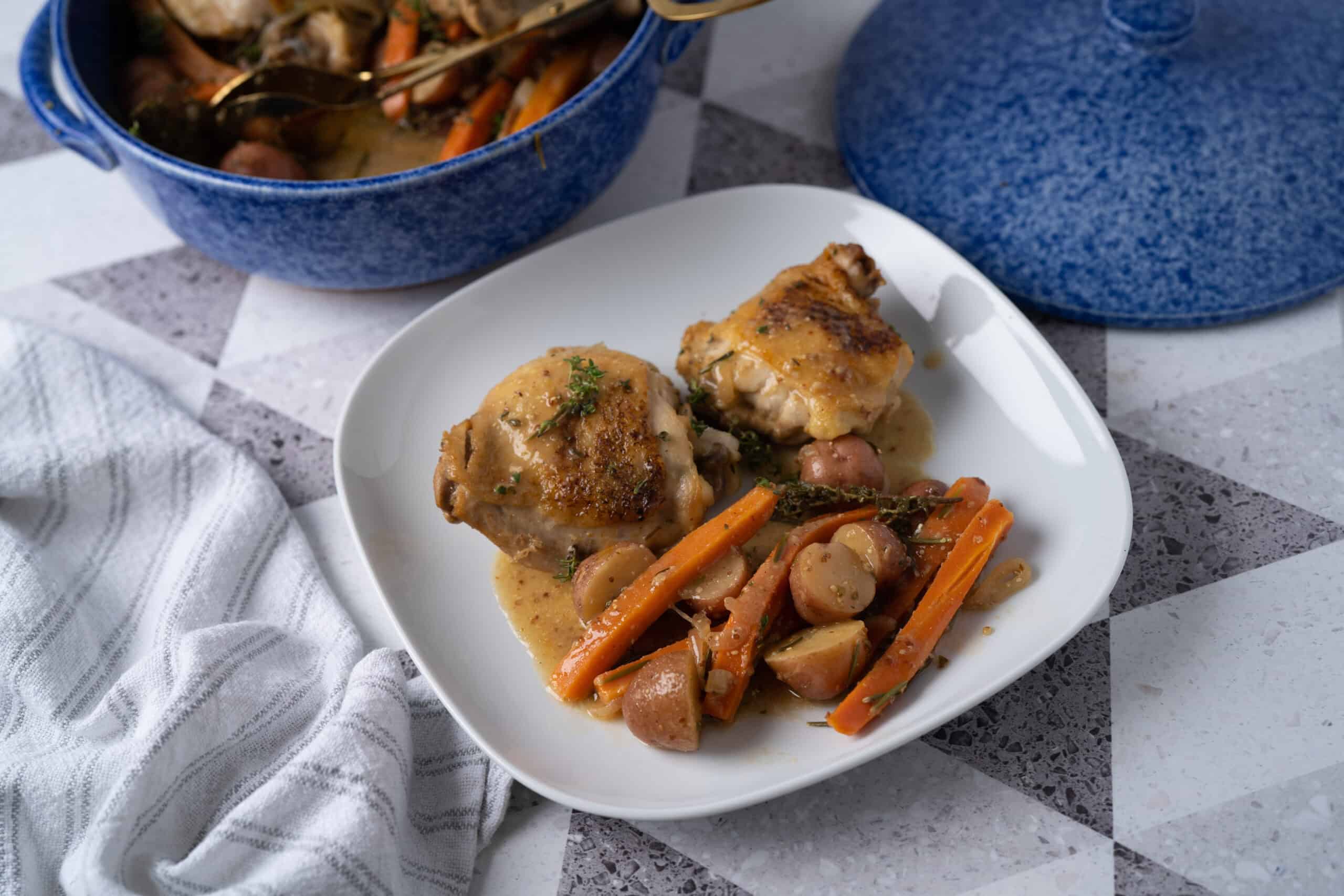 Succulent roasted chicken thighs with savory herb seasoning served with a hearty medley of carrots, potatoes, and mushrooms in a flavorful sauce on a white plate.