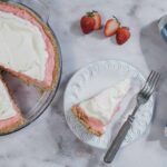 Buttercream strawberry pie, homemade strawberry pie with whipped cream topping, easy dessert recipe, fresh strawberries, baked pie with crumb crust, summer berry dessert, no-bake fruit pie, stylish white plate, blue striped napkin, rustic kitchen setting, sweet and tangy fruit dessert.