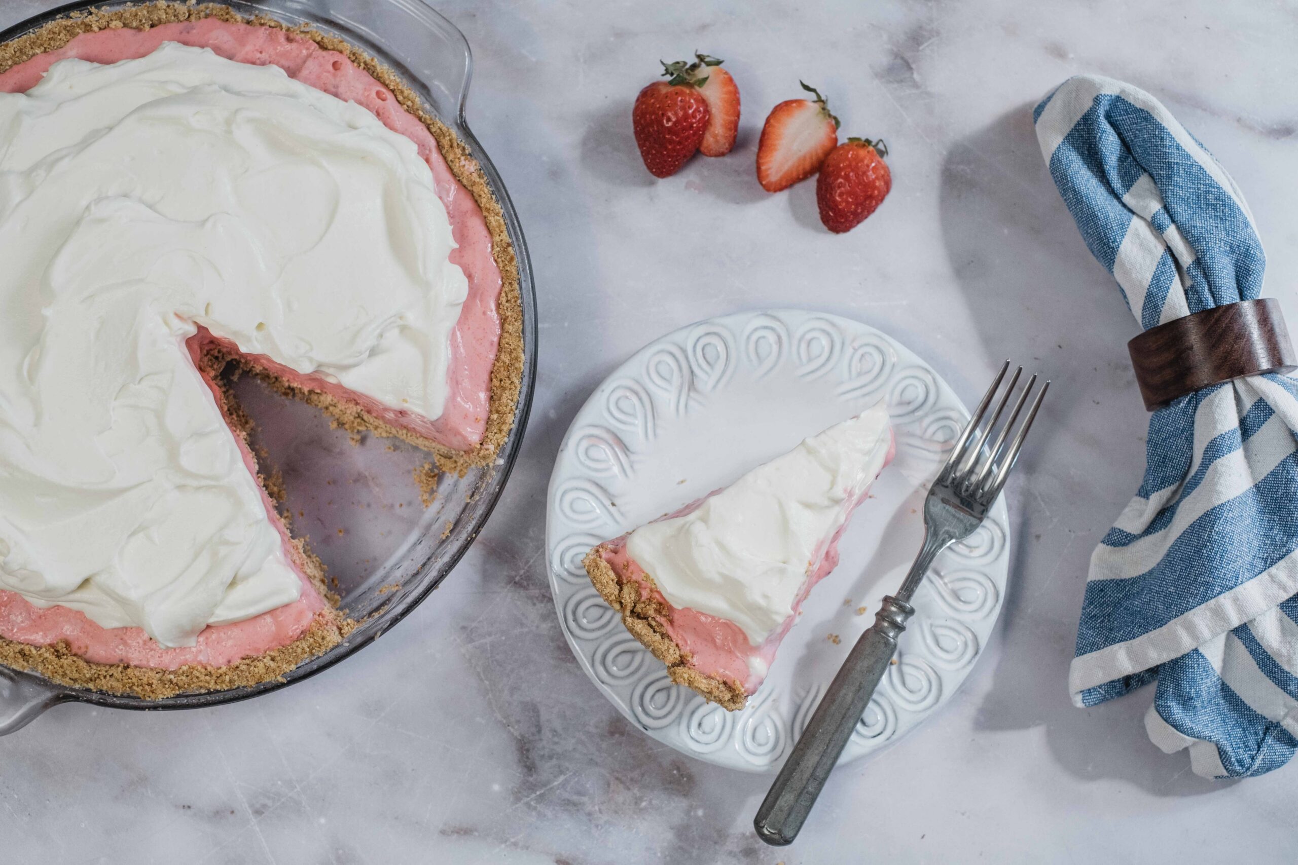 Buttercream strawberry pie, homemade strawberry pie with whipped cream topping, easy dessert recipe, fresh strawberries, baked pie with crumb crust, summer berry dessert, no-bake fruit pie, stylish white plate, blue striped napkin, rustic kitchen setting, sweet and tangy fruit dessert.