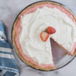 Light strawberry cream pie with whipped topping and fresh strawberry garnish on a glass pie dish.