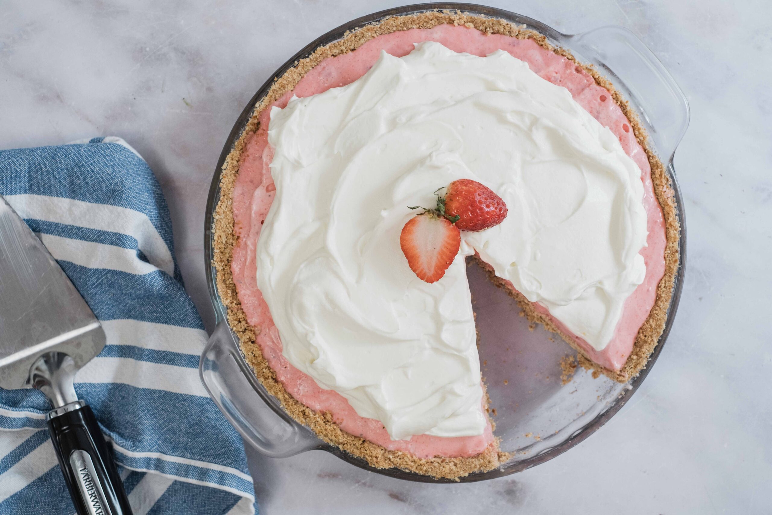 Light strawberry cream pie with whipped topping and fresh strawberry garnish on a glass pie dish.