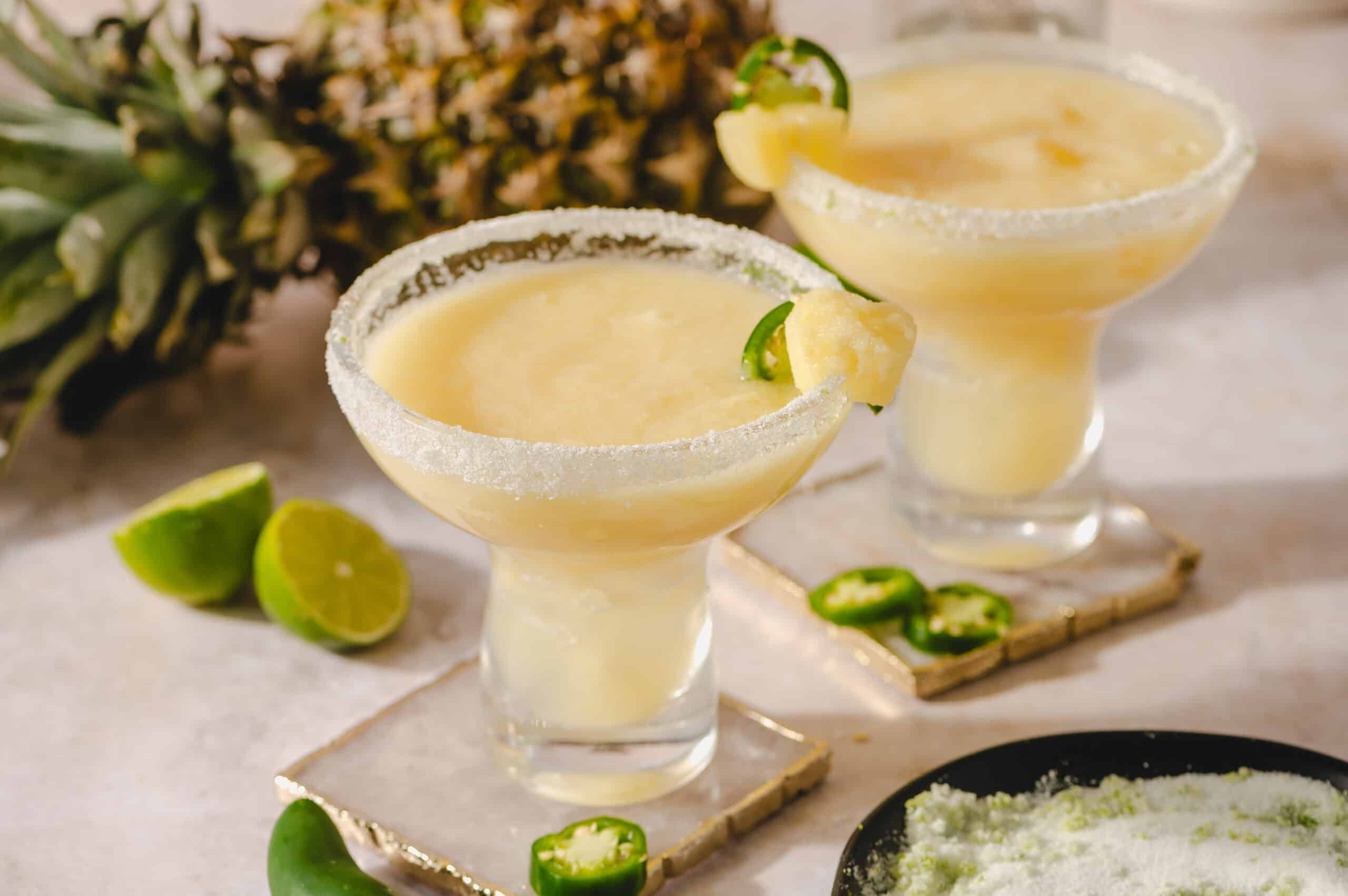 Refreshing pineapple margarita cocktails garnished with lime and jalapeño slices, served in salted rim glasses, perfect for summer parties and tropical vacations.