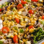Fresh taco salad with ground beef, cherry tomatoes, avocado, sweet corn, shredded cheese, and lettuce on a white platter. Perfect for healthy Mexican-inspired meal ideas.