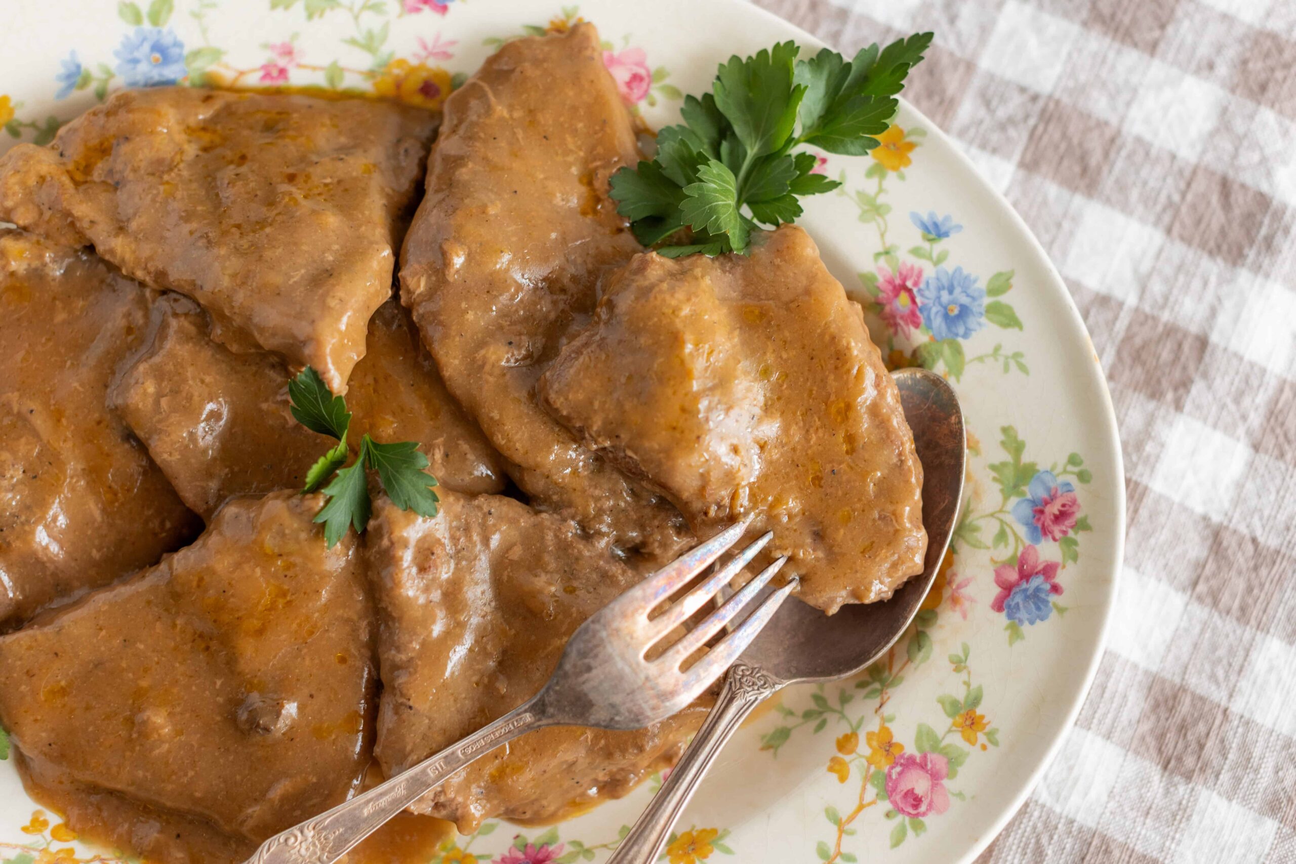 Savory beef stew with tender meat and rich gravy served on a floral plate garnished with fresh parsley. Perfect comfort food for family dinners and special occasions.