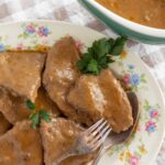 Succulent beef stew with tender chunks of meat covered in rich, savory gravy on a floral porcelain plate.