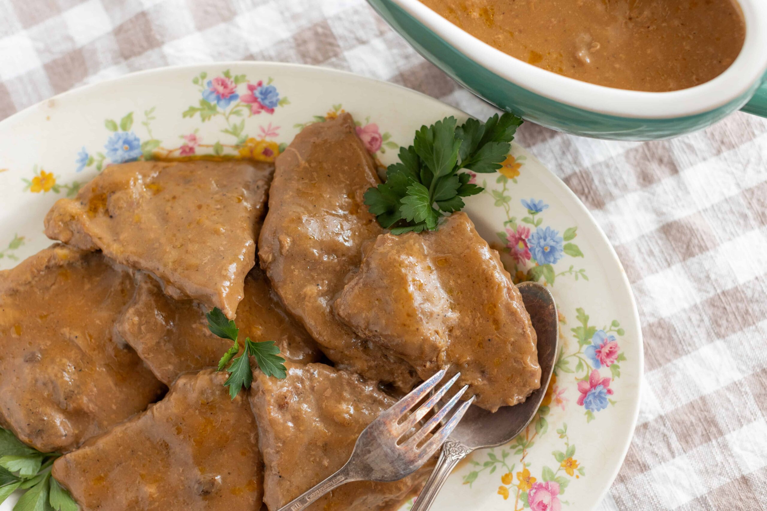 Succulent beef stew with tender chunks of meat covered in rich, savory gravy on a floral porcelain plate.