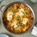Creamy baked lasagna in a stainless steel dish topped with melted cheese, fresh basil, and chopped herbs, served on a rustic kitchen countertop for a delicious Italian home-cooked meal.