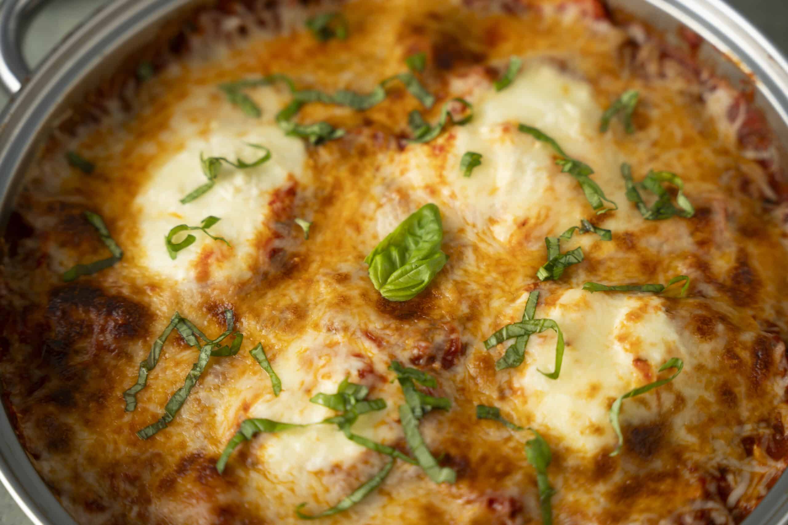 Golden baked lasagna with melted cheese, fresh basil, and chopped herbs, served in a round oven dish. Perfect for family dinners and comfort food lovers.