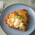 Tender baked lasagna with melted cheese and fresh basil garnish on a blue plate. Perfect comfort food for dinner, featuring rich tomato sauce, gooey cheese, and perfectly layered pasta.