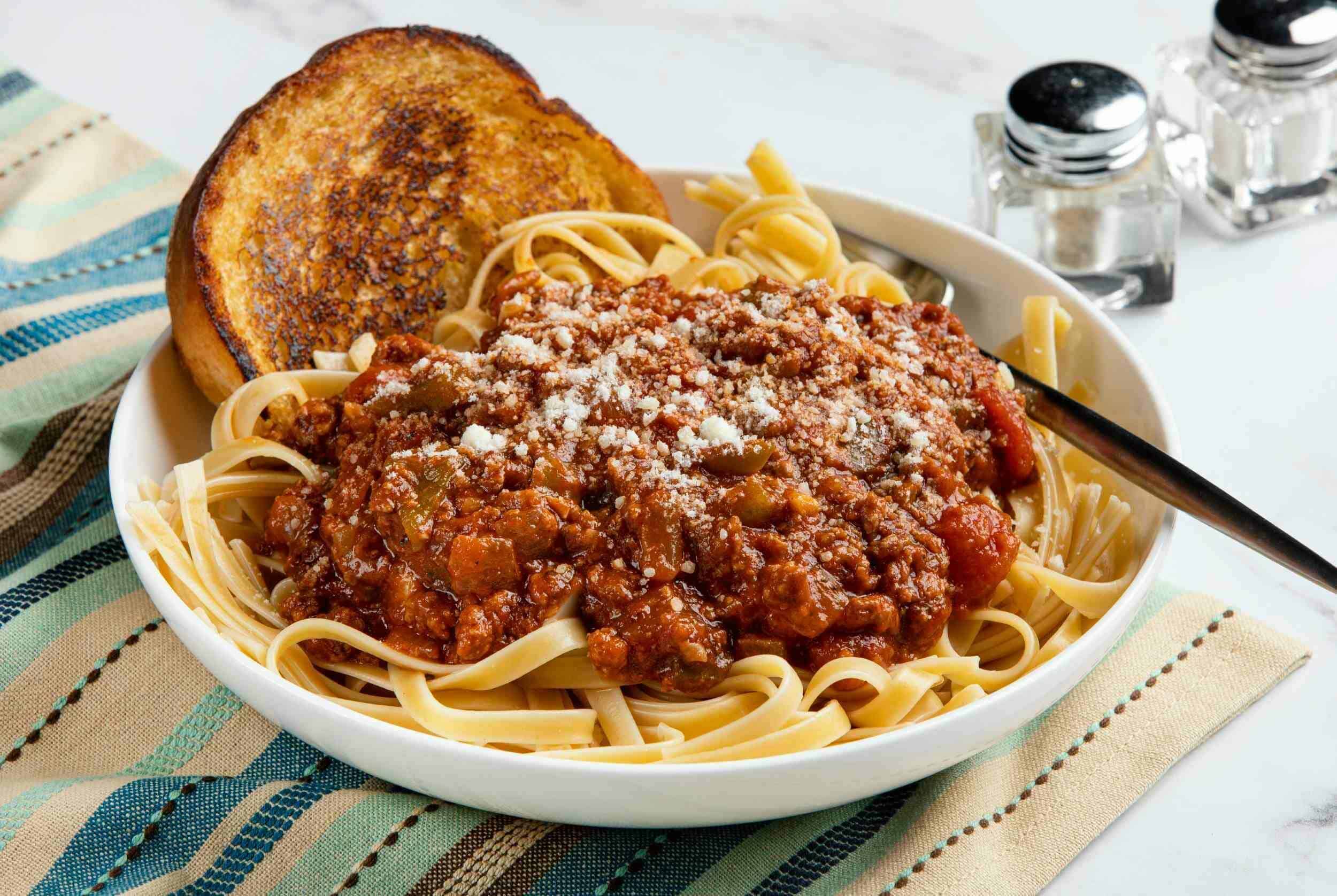 Creamy beef bolognese pasta served with garlic bread on a colorful striped napkin, highlighting a comforting homemade Italian meal perfect for family dinner nights.