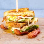 Crispy bacon, fried eggs, and fresh vegetables between two slices of toasted bread in a delicious breakfast sandwich. Perfect for brunch or a hearty meal.