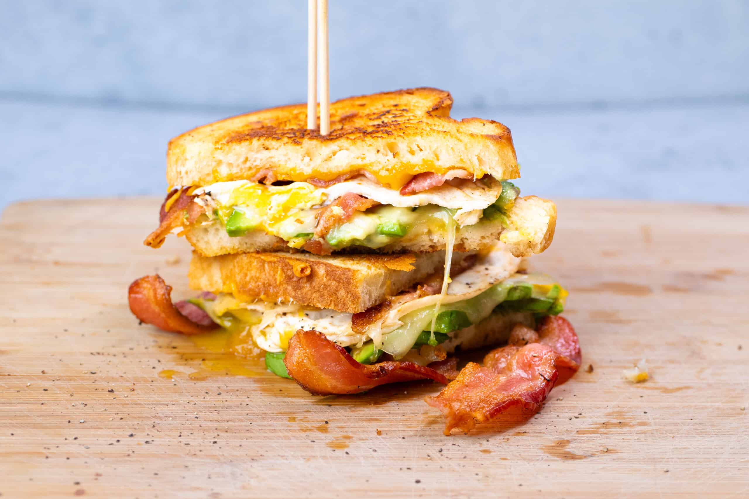 Crispy bacon, fried eggs, and fresh vegetables between two slices of toasted bread in a delicious breakfast sandwich. Perfect for brunch or a hearty meal.