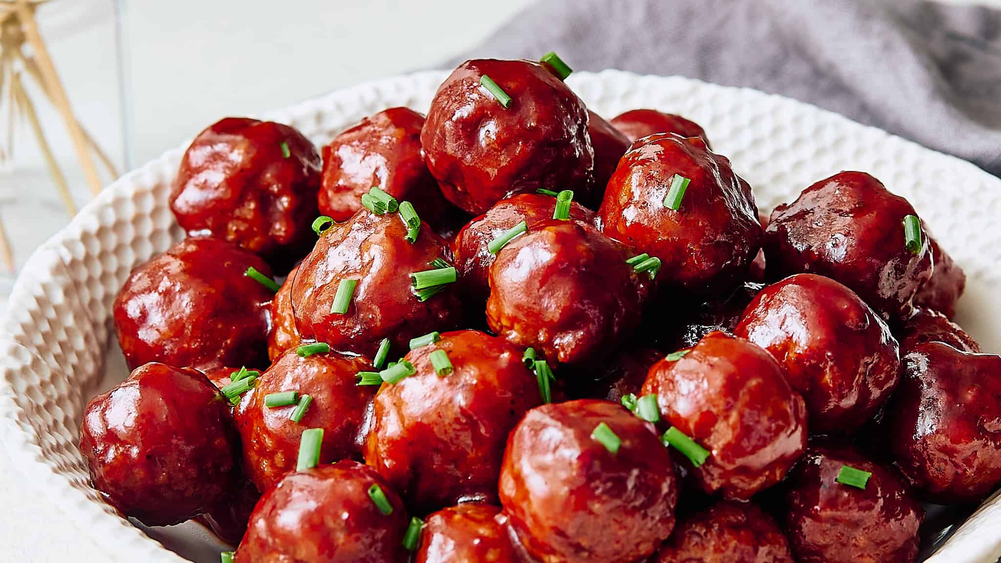 Savory glazed meatballs garnished with chopped green onions on a white textured plate, perfect for homemade dinner or party appetizers.