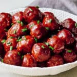 Savory glazed meatballs garnished with chopped green onions served in a textured white bowl. Perfect for easy appetizers or comforting family meals.