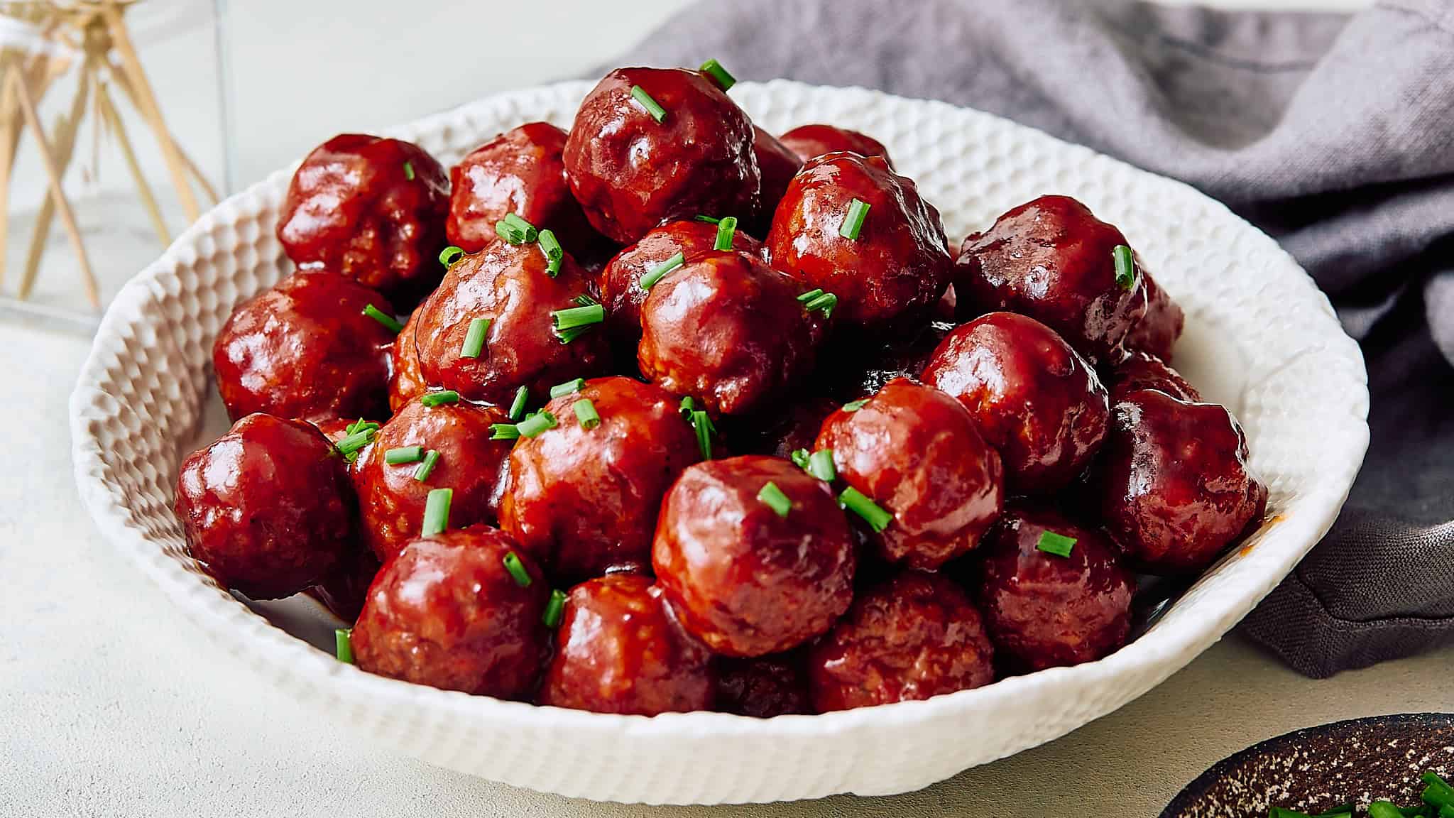 Savory glazed meatballs garnished with chopped green onions served in a textured white bowl. Perfect for easy appetizers or comforting family meals.
