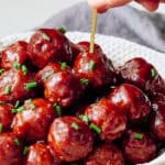 Meatballs glazed with sauce garnished with chopped chives in a white textured bowl.