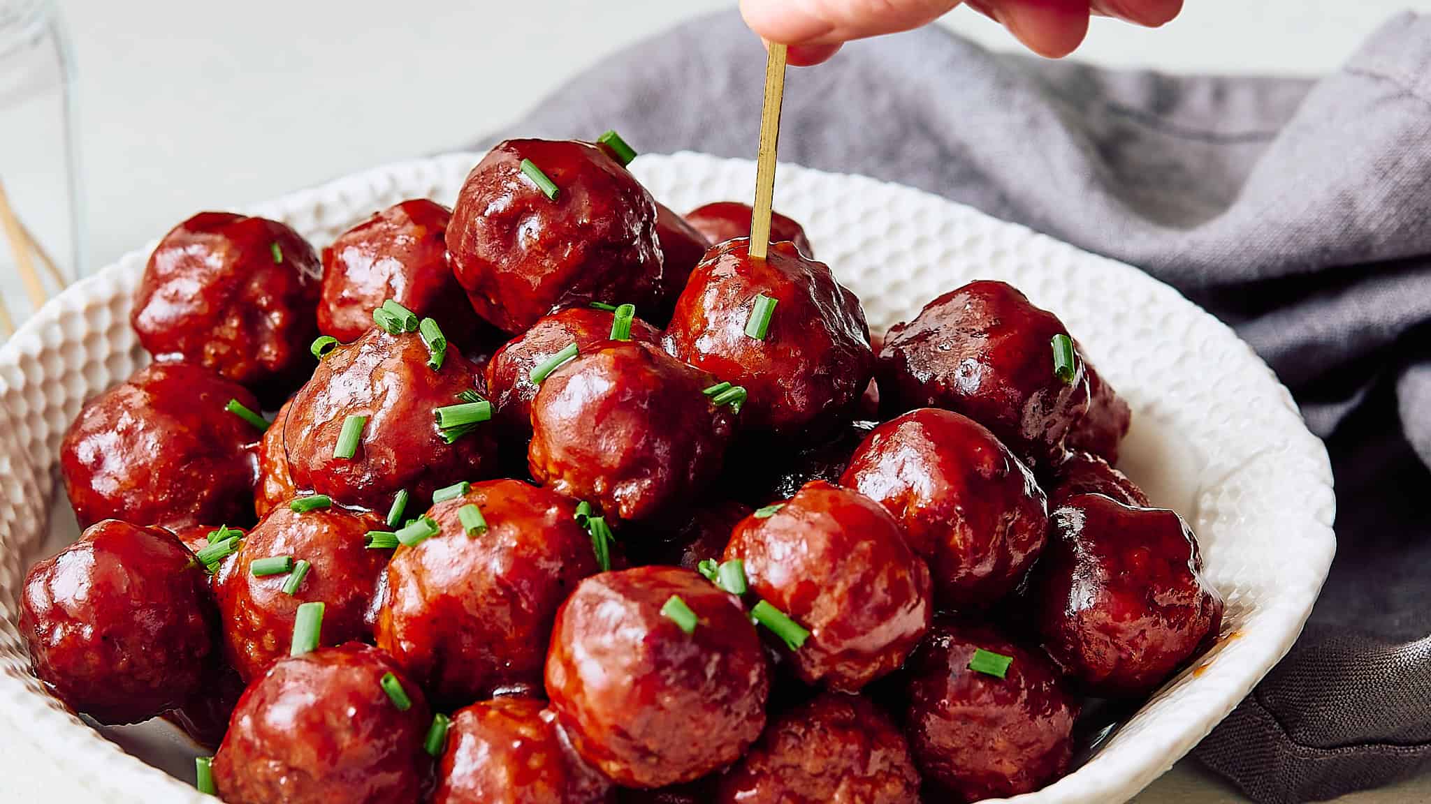 Meatballs glazed with sauce garnished with chopped chives in a white textured bowl.