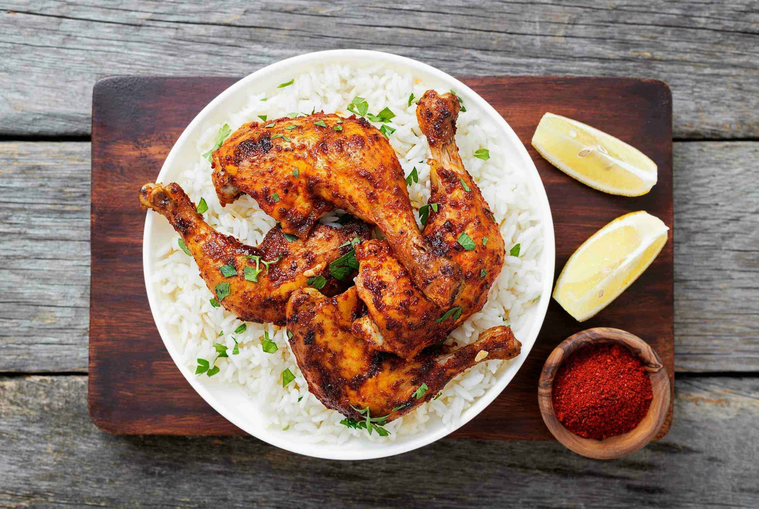 Succulent grilled chicken thighs served over fluffy white rice, garnished with fresh herbs, accompanied by lemon wedges and vibrant red spice for a flavorful meal.