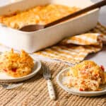 Creamy chicken casserole topped with melted cheese, served on white plates with a fork, set on a textured placemat in front of a baking dish of hot chicken casserole with a wooden spoon, featuring a cozy, home-cooked meal perfect for family dinner.